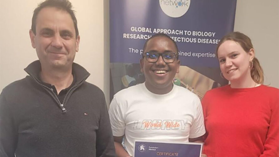 Three people are standing in front of a roll-up bearing the logo of the GABRIEL Network; the person in the middle is holding the training certificate in his hands.